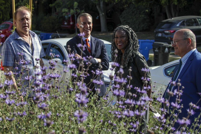 Four people stand outside behind purple flowers.