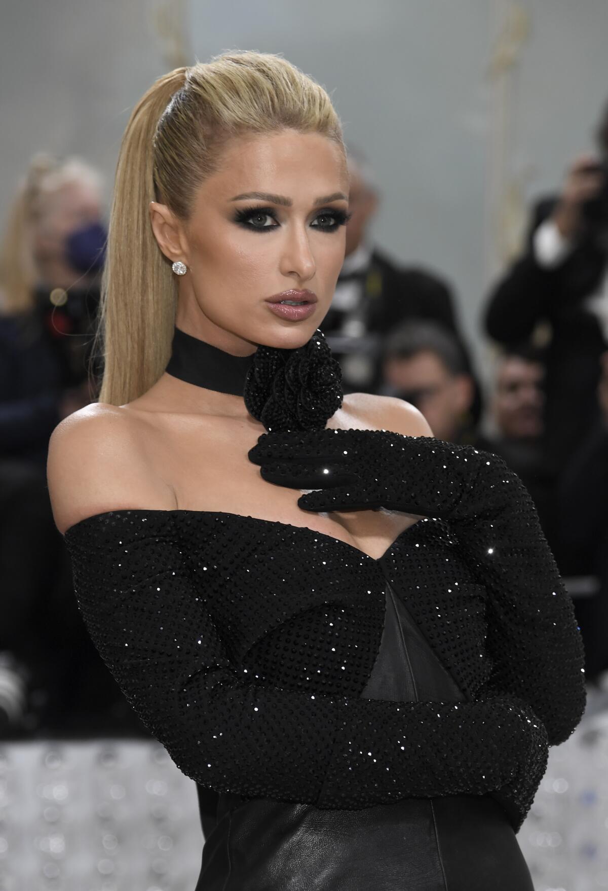 Paris Hilton attends the Met Gala in a strapless black gown, holding one gloved hand to her chest