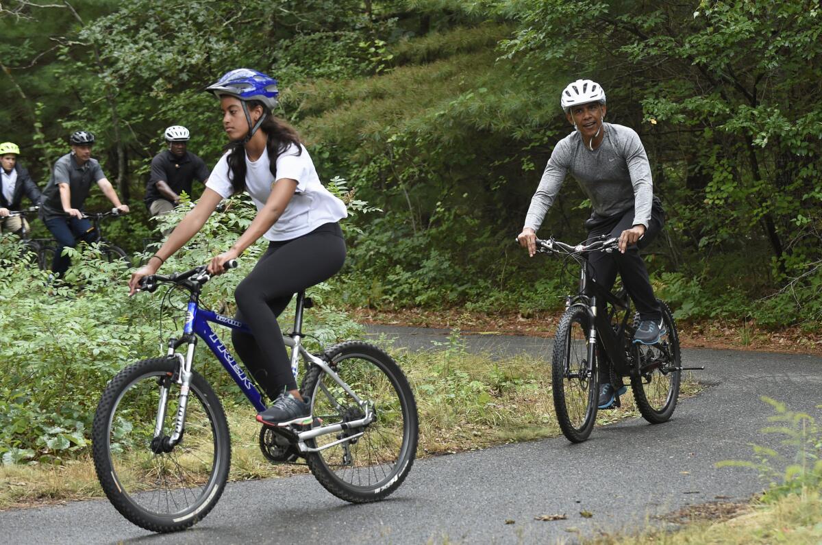 President Barack Obama, right, rides a bike with his daughter Malia, left, in West Tisbury, Mass., on Martha's Vineyard, Saturday, Aug. 22, 2015. Obama and his family vacation every August on Martha's Vineyard. (AP Photo/Susan Walsh)