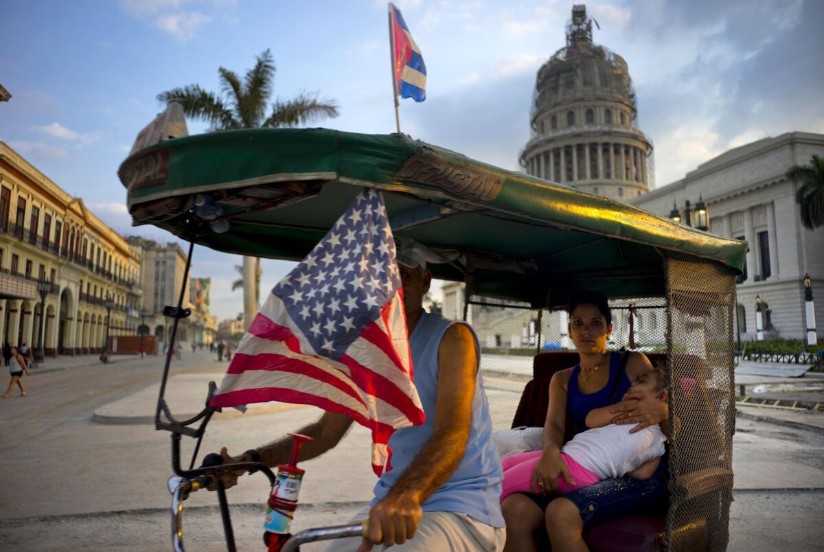 A taxi pedals his bicycle, decorated with Cuban and U.S. flags, as he transports a woman holding a sleeping girl, near the Capitolio in Havana, Cuba.