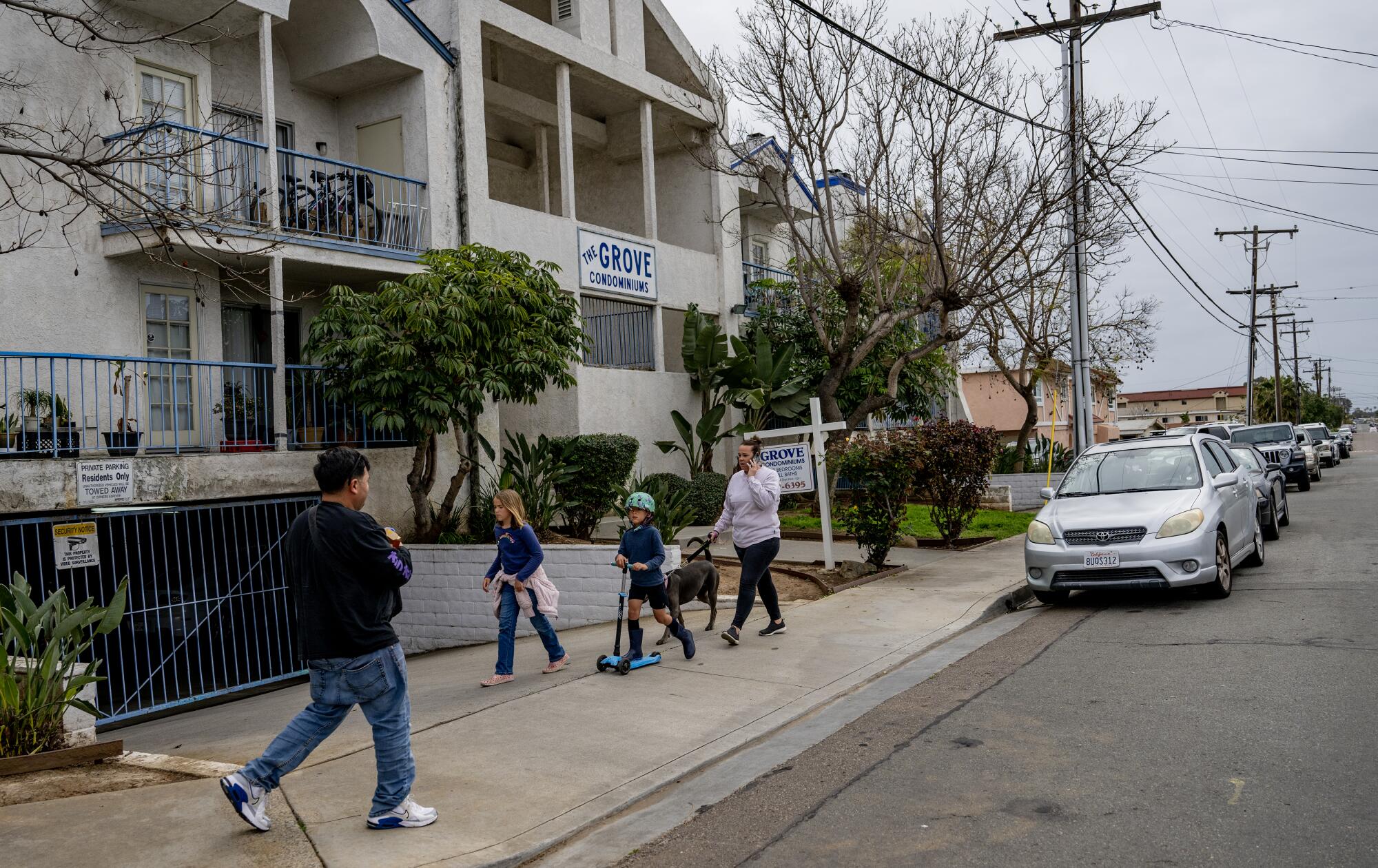 Pedestrians walk along a sidewalk outside an apartment building.