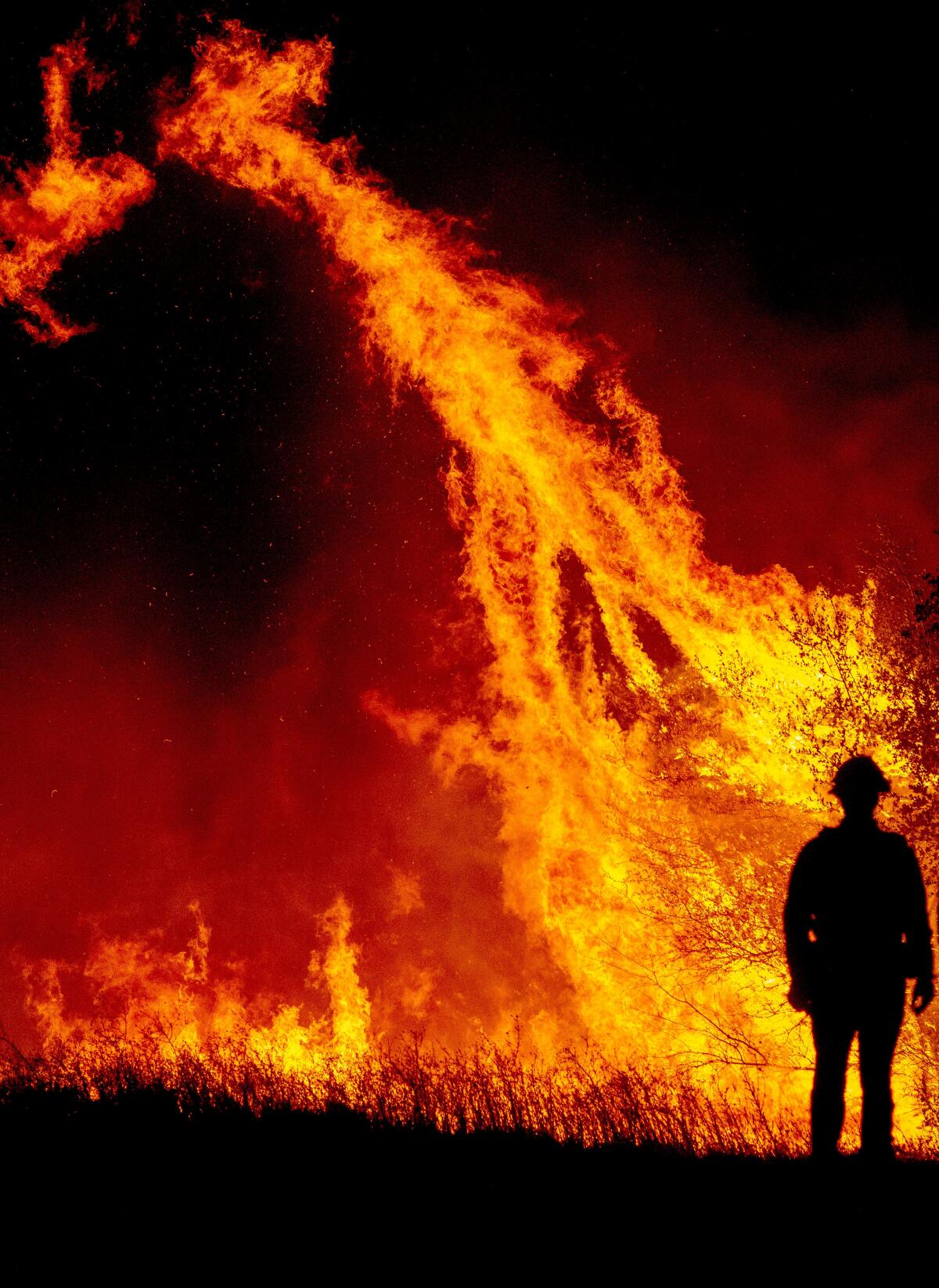 A firefighter is silhouetted against a wall of orange flame