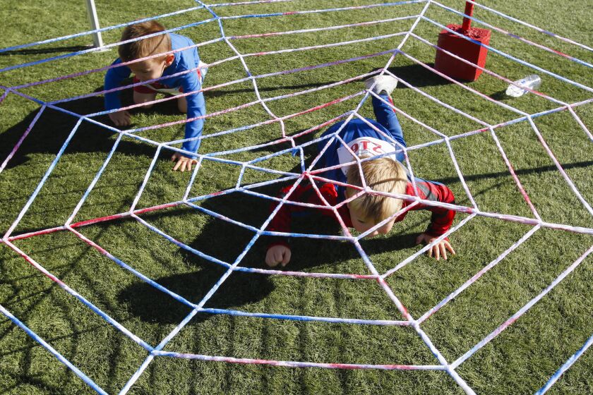 More than 400 children and parents took part in the annual 2019 Supper Hero obstacle challenge at Alga Norte Community Park in Carlsbad. Two super heroes crawl under a large spider web at the Web Crawler obstacle.