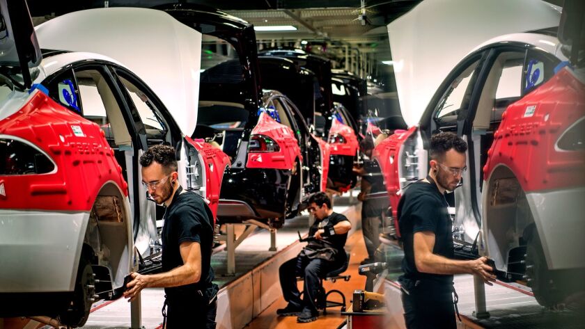 A worker is reflected in a computer screen as he and others assemble cars on the line at Tesla's factory in Fremont.