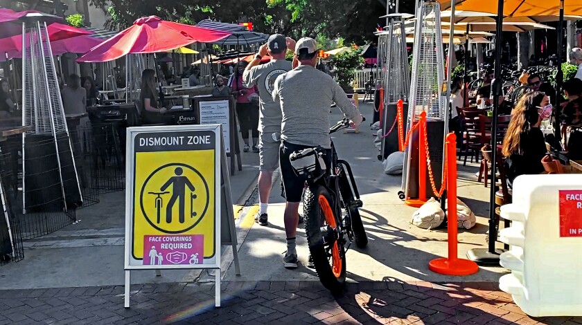 Pedestrians and cyclists share a pathway between outdoor dining areas in Santa Barbara
