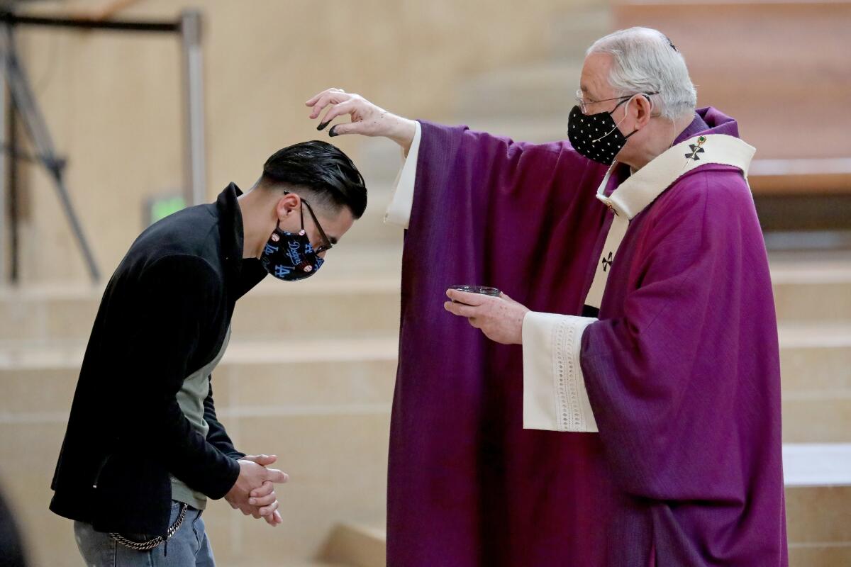Archbishop José Gomez raises his hand above a bowed parisioner with clasped hands