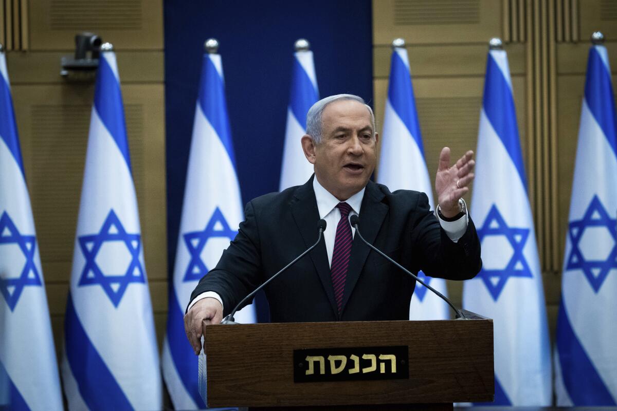 Israeli Prime Minister Benjamin Netanyahu stands at a lectern in front of Israeli flags.