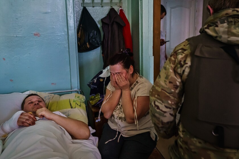 Oksana Seychuk couvre son visage et pleure sur pleure à côté du lit de son mari blessé. 