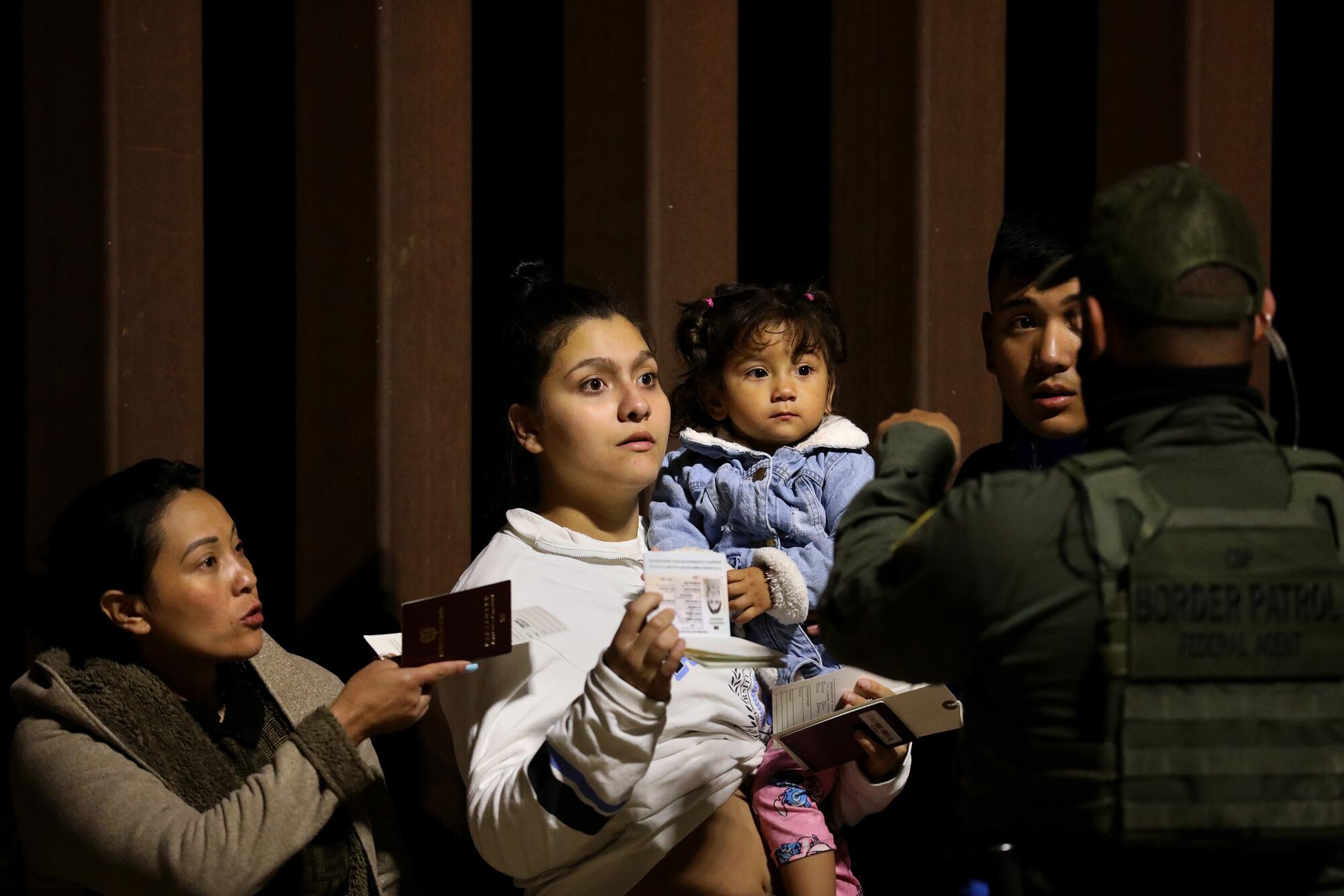 A man and two women, one holding a toddler, show passports to a border agent