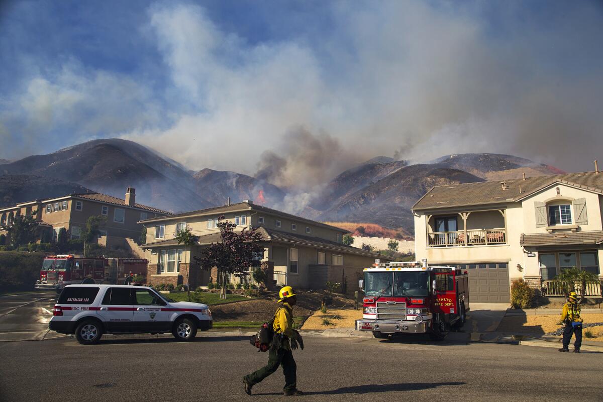 A plane drops fire retardant near homes to keep the fast-moving Mart fire from approaching from the hillsides near Highway 330 in Highland, Calif.