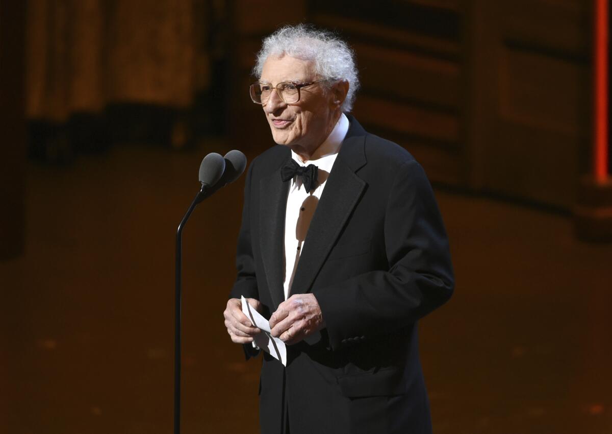 A man in a tuxedo stands at a microphone.