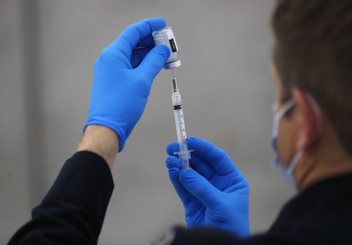 Gloved hands prepare a vaccine syringe 