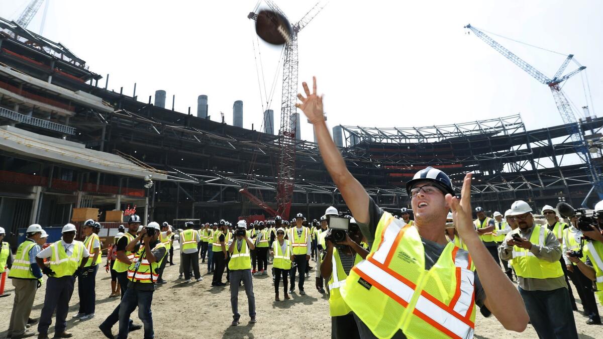 Rams quarterback Jared Goff tosses a football up to construction workers during a June 14 tour of a new stadium under construction in Inglewood.