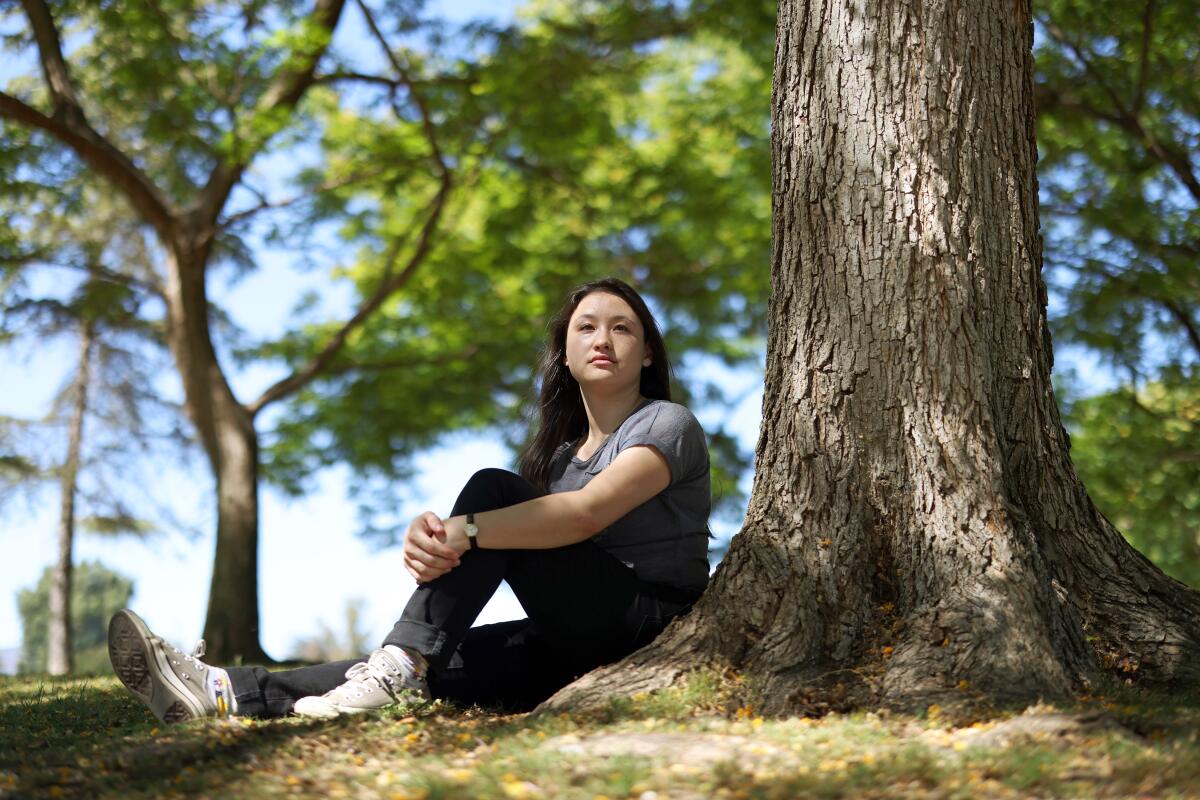 Rebecca Nathan sits next to a tree trunk