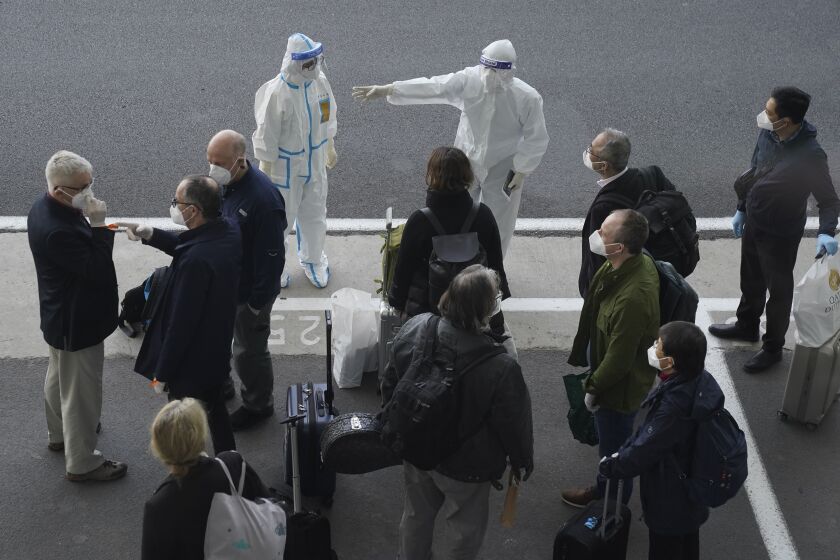 A worker in protective coverings directs members of the World Health Organization (WHO) team on their arrival at the airport in Wuhan in central China's Hubei province on Thursday, Jan. 14, 2021. A global team of researchers arrived Thursday in the Chinese city where the coronavirus pandemic was first detected to conduct a politically sensitive investigation into its origins amid uncertainty about whether Beijing might try to prevent embarrassing discoveries. (AP Photo/Ng Han Guan)