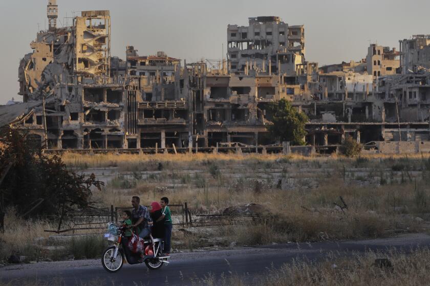 ARCHIVO - Personas en motocicleta pasan junto a edificios destrozados, el 15 de agosto de 2018, en la parte antigua de la ciudad de Homs, Siria. (AP Foto/Sergei Grits, Archivo)