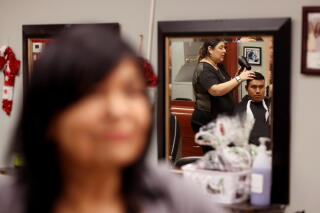 A woman, with a mirror in the background showing a person using a hair dryer on another person's head.