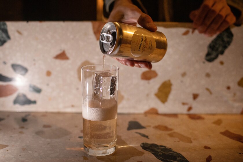 A cocktail in a can is poured into a highball glass on a terrazzo bar.