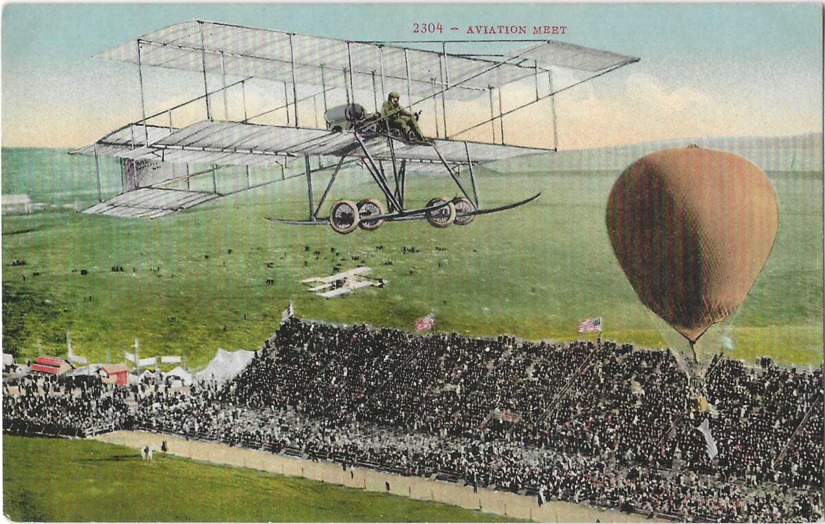 An airplane and an orange hot air balloon over a green field and a packed grandstand