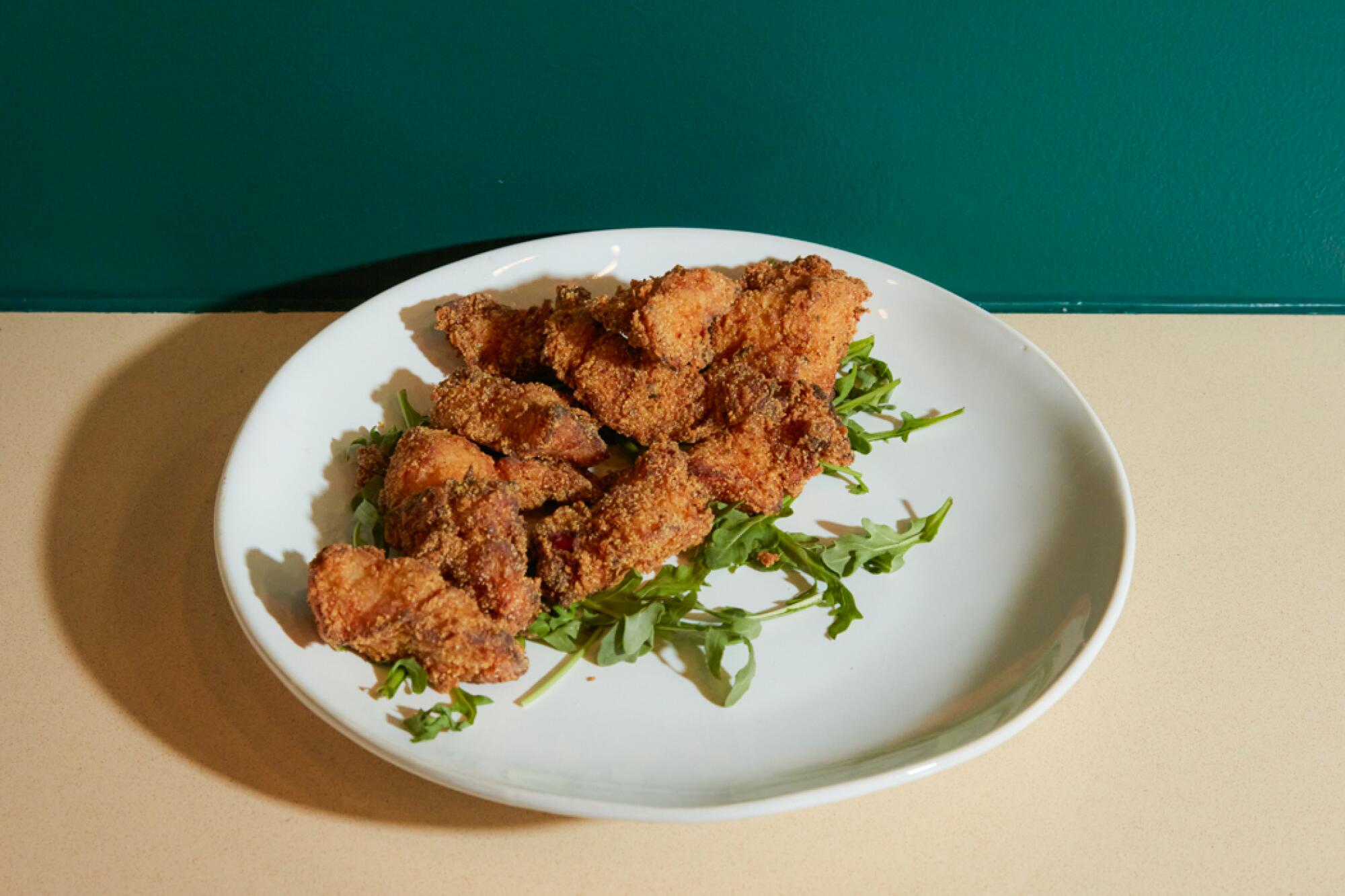 A small pile of rockfish nuggets atop arugula on a white plate against a green wall