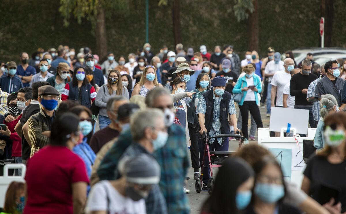 People with masks stand in line in a parking lot