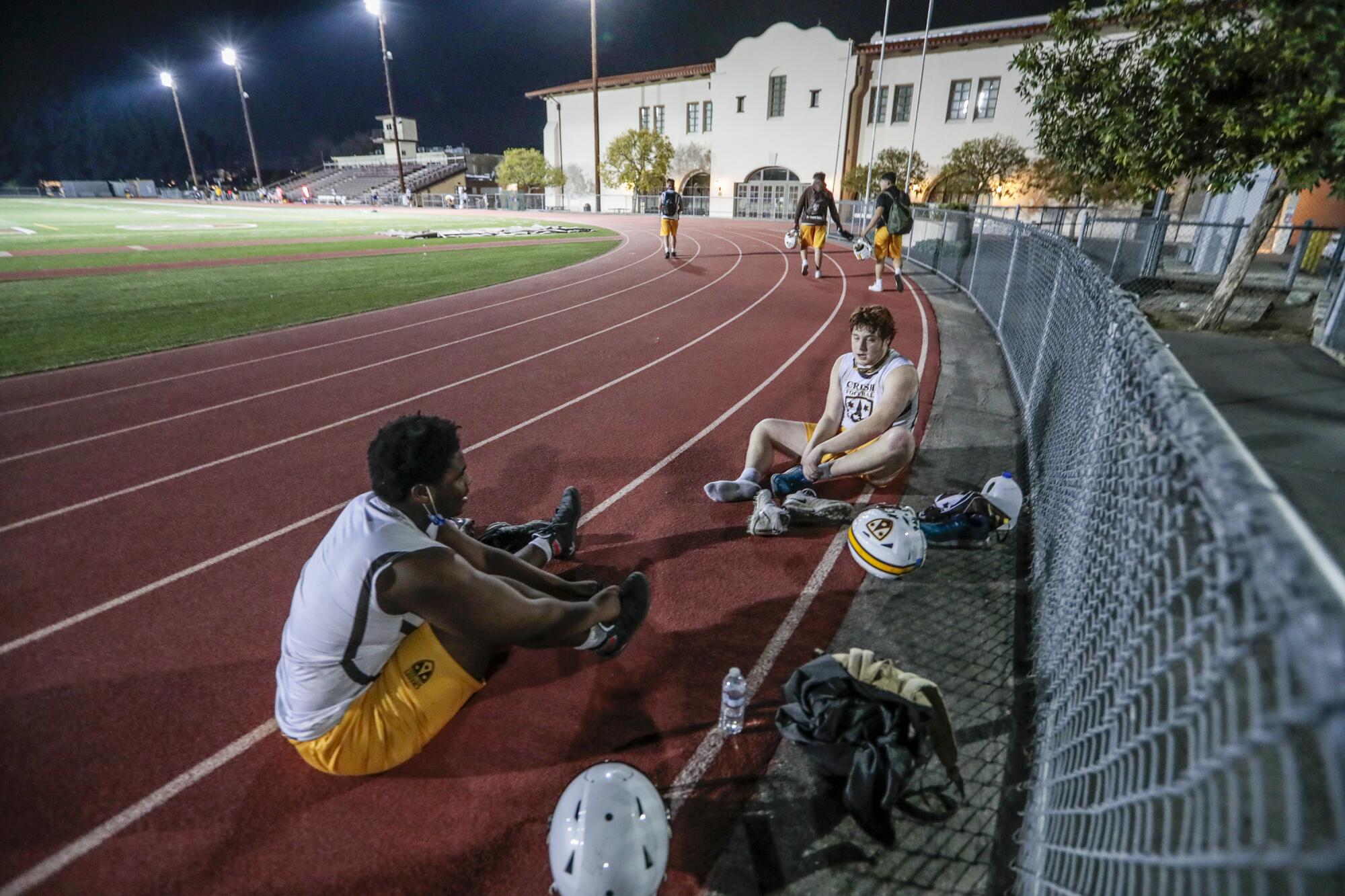 Kaliq Wilkens and Anthony Calfo change their shoes on the track following practice at Crespi High.