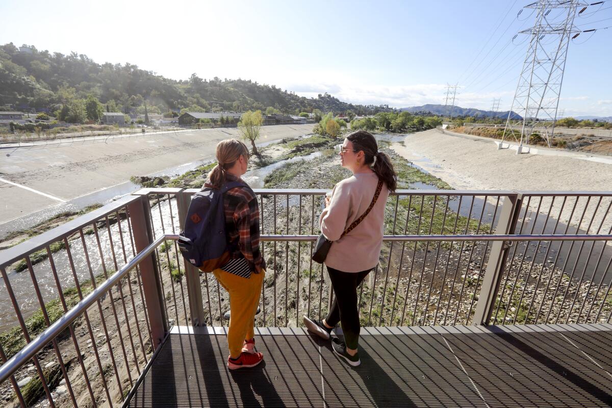 Two people converse on an observation deck over a river.