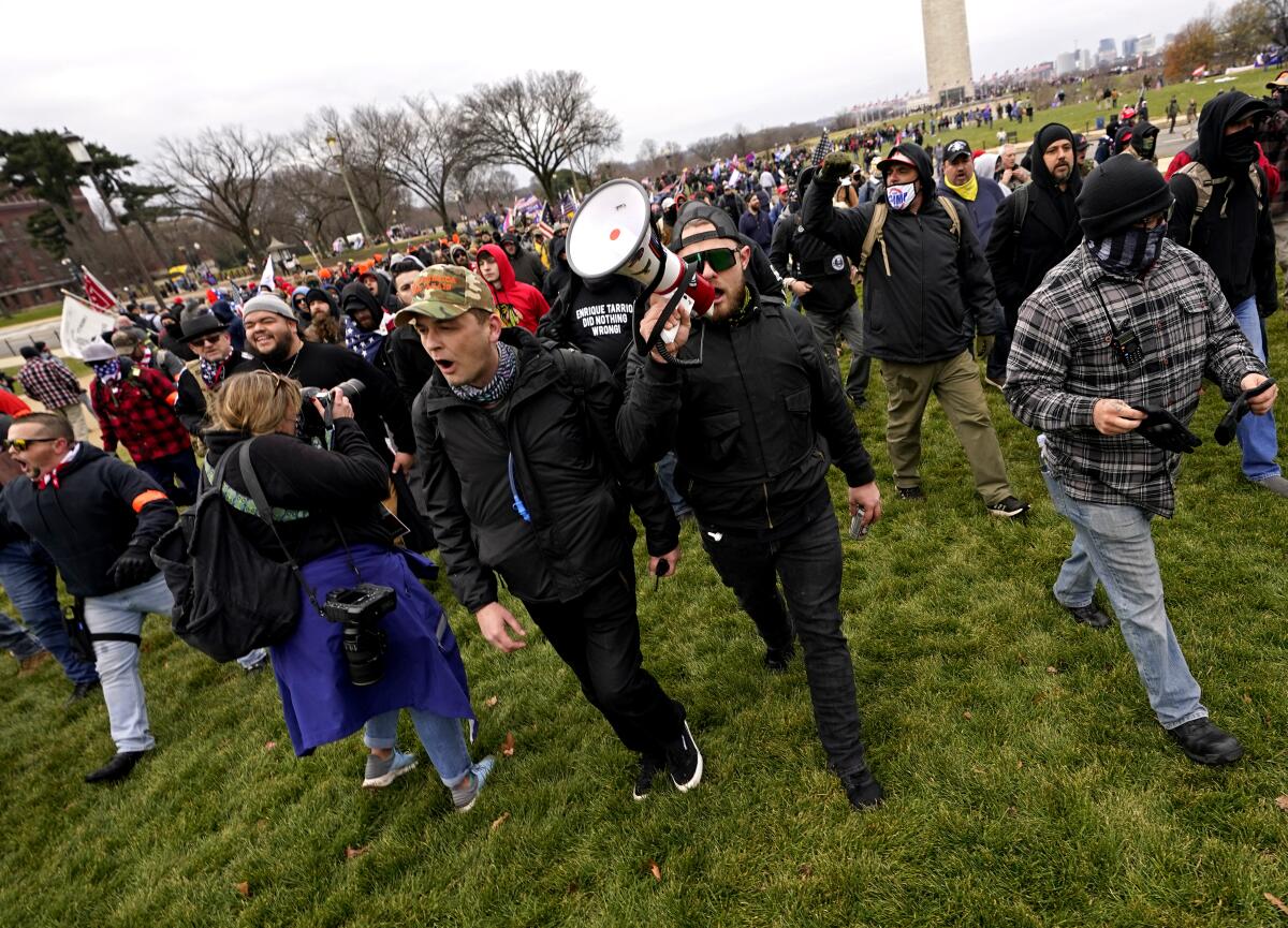 A man with a bullhorn leads a large group of men dressed in black across a lawn.