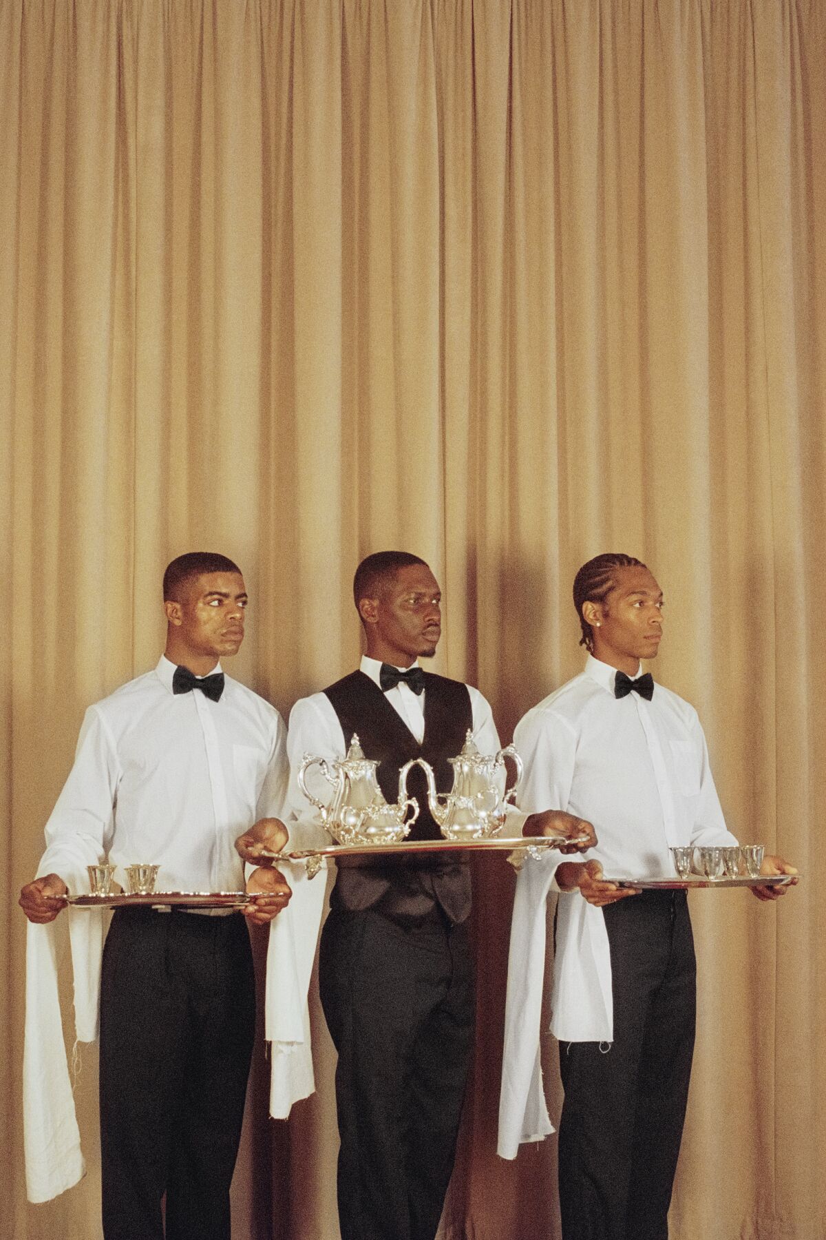 An image of three men holding trays in front of a beige curtain.