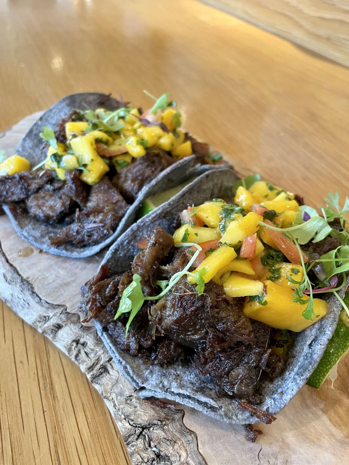 Two beef rendang tacos in blue cornbread, topped with mango sambal sauce.