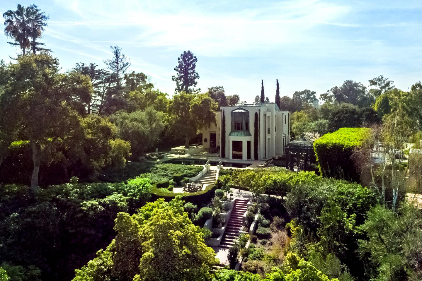 An aerial view of the home's exterior shows a swimming pool and steps leading down to formal gardens with lush trees