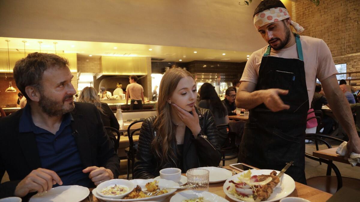 Phil Rosenthal, left, of Netflix's "Somebody Feed Phil," and daughter Lily listen as Bavel chef Ori Menashe describes the half duck dish of aged breast kebab, confit leg, bone broth, green amba and chicory salad.