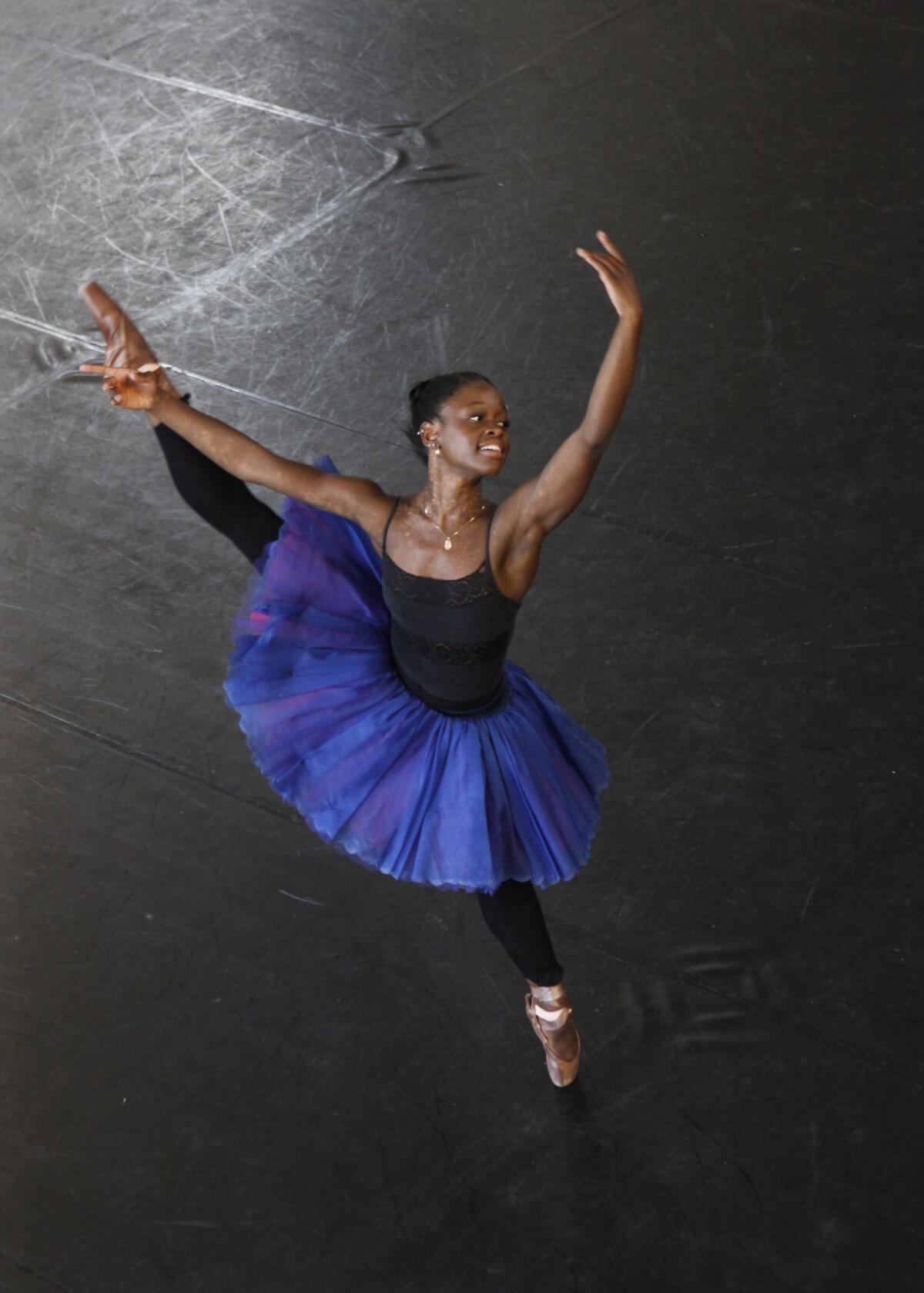 Michaela DePrince leaping in ballet gear and a blue tutu extending her right leg and raising her left arm