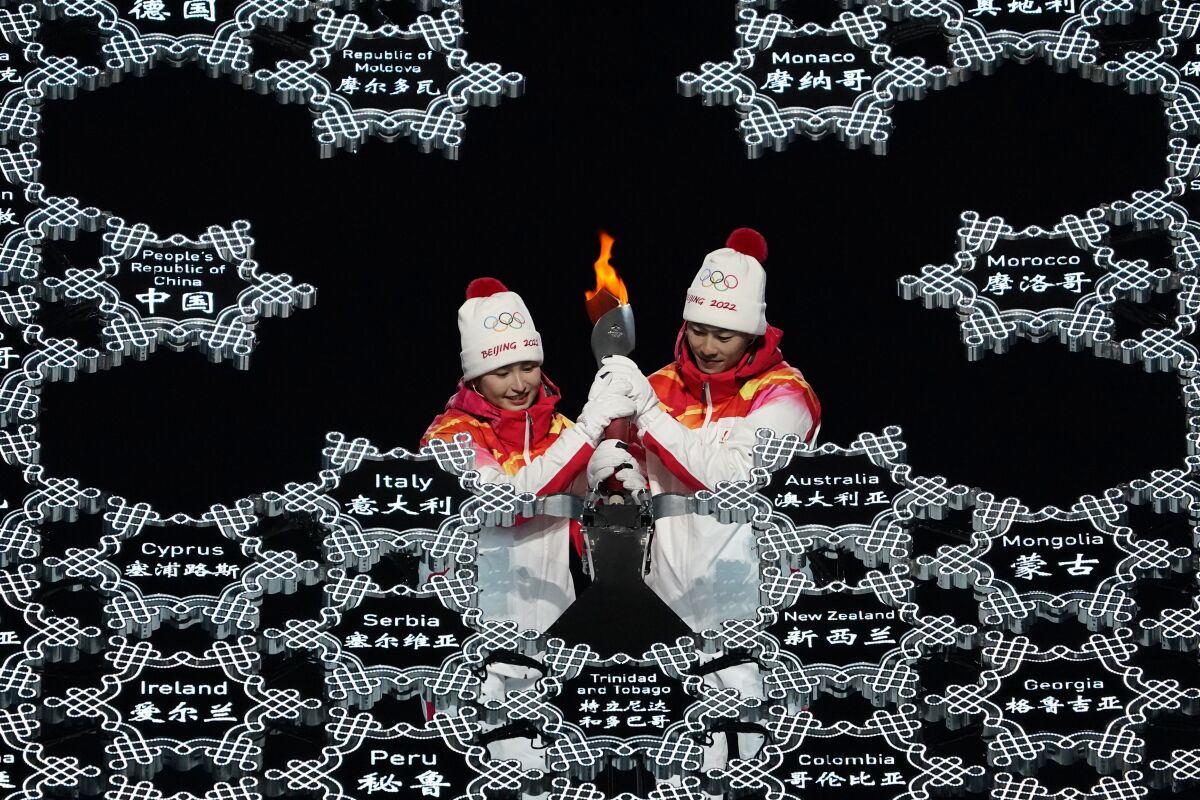 Two people in Olympics outfits light the cauldron during the opening ceremony of the Winter Olympics.