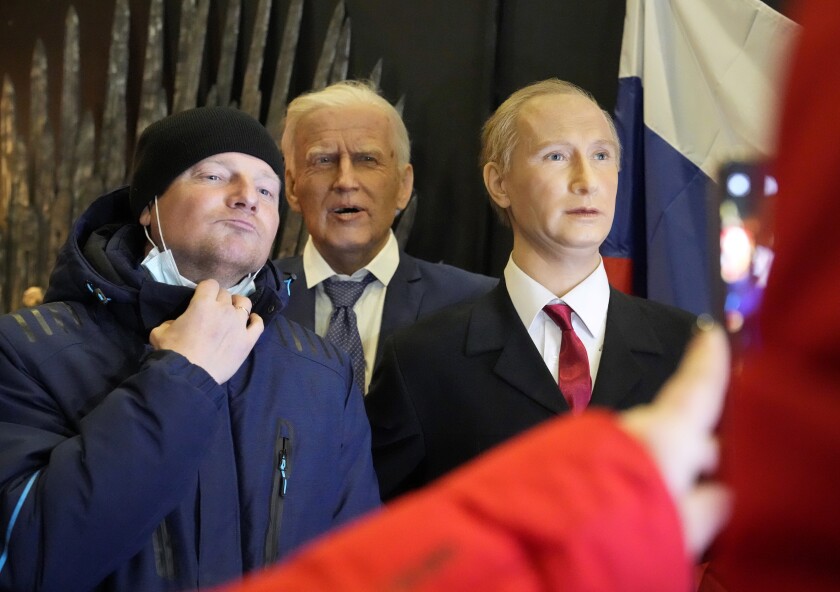 A man poses for photo next to wax figures depicting U.S. President Joe Biden and Russian President Vladimir Putin displayed at a wax sculptures exhibition in St. Petersburg, Russia, Monday, Dec. 6, 2021. President Joe Biden and Russian President Vladimir Putin will speak in a video call Tuesday as tensions between the U.S. and Russia escalate over a Russian troop buildup on the Ukrainian border seen as a sign of a potential invasion. (AP Photo/Dmitri Lovetsky)