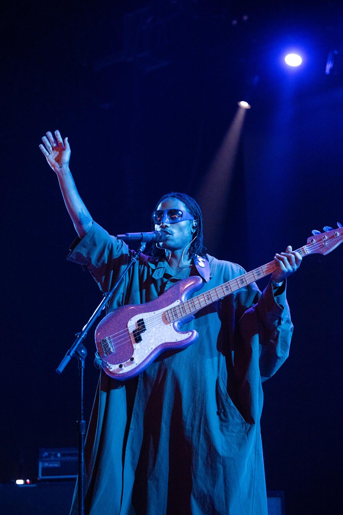 A musician in a long robe performs onstage with an electric guitar