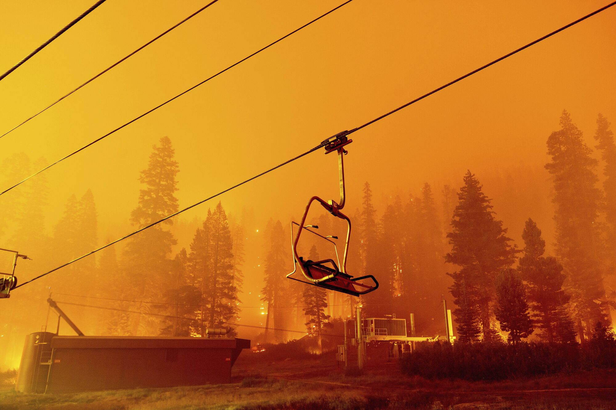 An empty chair lift against a backdrop of trees, flames and smoke.
