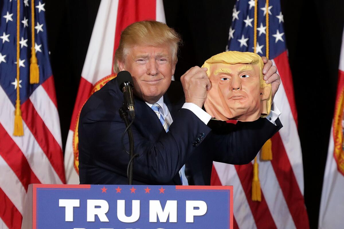 Donald Trump holds a rubber mask of himself.