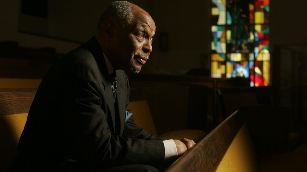 The Rev. Cecil L. Murray sits in a church pew, a colorful stained-glass window in the background