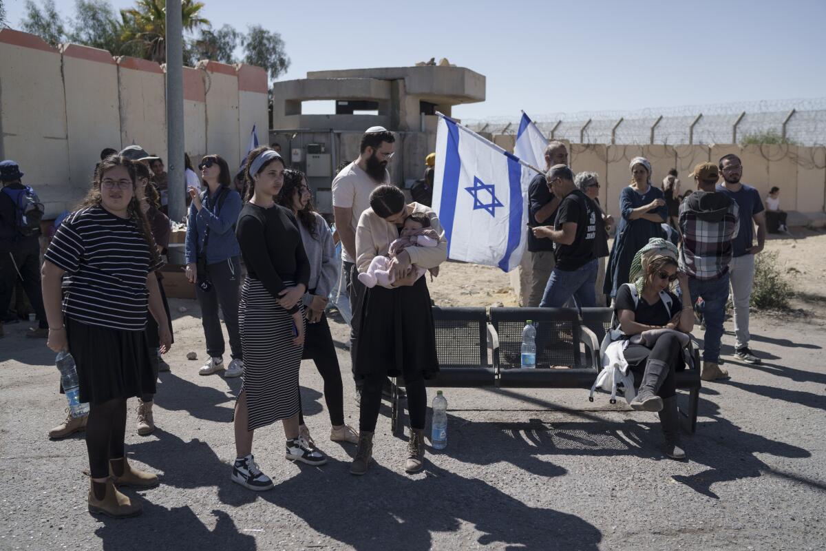 Protesters, some carrying a blue-and-white flag with a blue star, gather at a fenced area