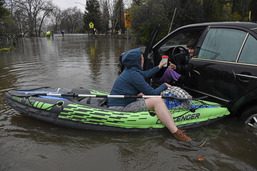 Nurse Katie Leonard, left, hands a cup of hot tea to Patsy Costello, 88, as she sits trapped in her vehicle for over an hour on Astrid Drive in Pleasant Hill, Calif., on Saturday, Dec. 31, 2022. Costello drove her car on the flooded street thinking she could make it when it stalled in the two feet of water. After two hours the water had receded about a foot making it easier to rescue her. Police were called but stood by and watched after calling in a tow truck to help pull the car out of the water. Nurse Katie Leonard, of Pleasant Hill, lives down the block used her kayak to bring Costello hot tea, blankets, food and a phone to call a friend. (Jose Carlos Fajardo/Bay Area News Group via AP)