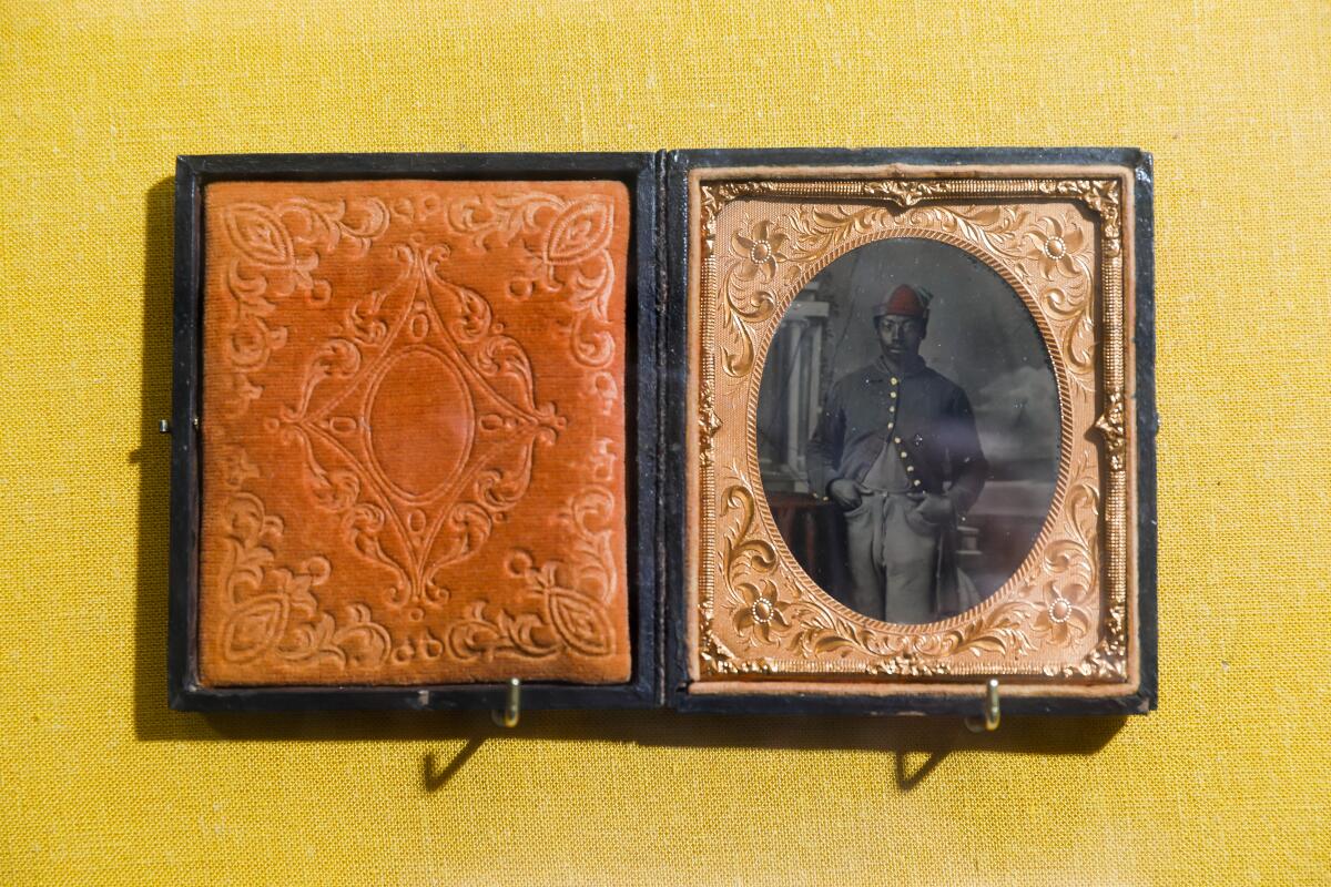 A tintype photograph of a Black soldier in Union garb is presented in an ornate frame is presented in a vitrine