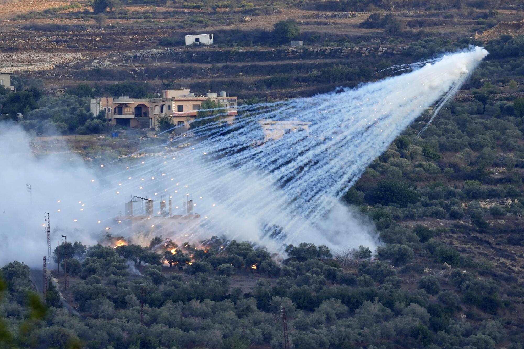 A shell that appears to be white phosphorus from Israeli artillery explodes over homes and farmland.