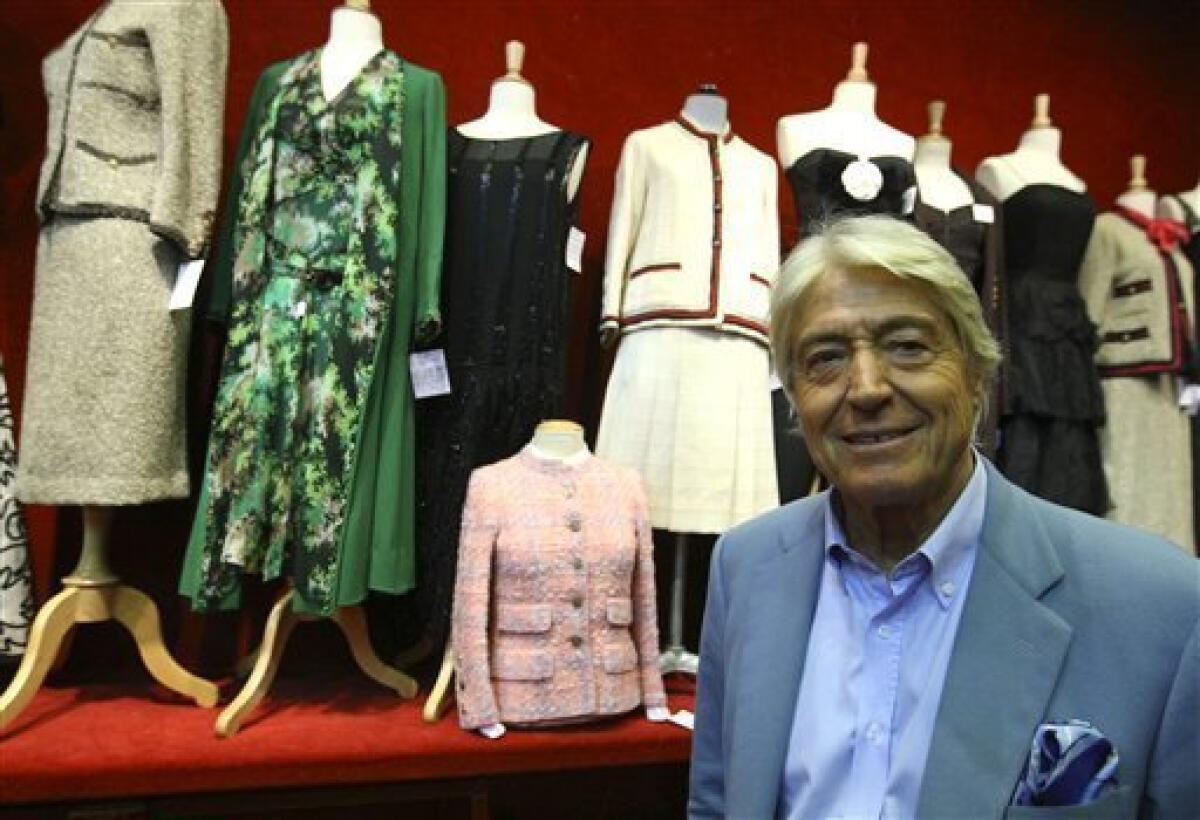 Auction officer Pierre Cornette de Saint Cyr poses next to Chanel outfits at a Paris auction house, Thursday Feb. 25, 2010. Some 600 garments, accessories and shoes by the storied luxury giant Chanel hit Paris' auction blocks, with lots at the two-day-long sale including haute couture dresses designed by Mademoiselle Chanel herself. (AP Photo/Jacques Brinon)