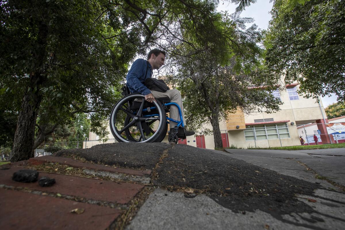 David Radcliff crossing a warped sidewalk in his wheelchair