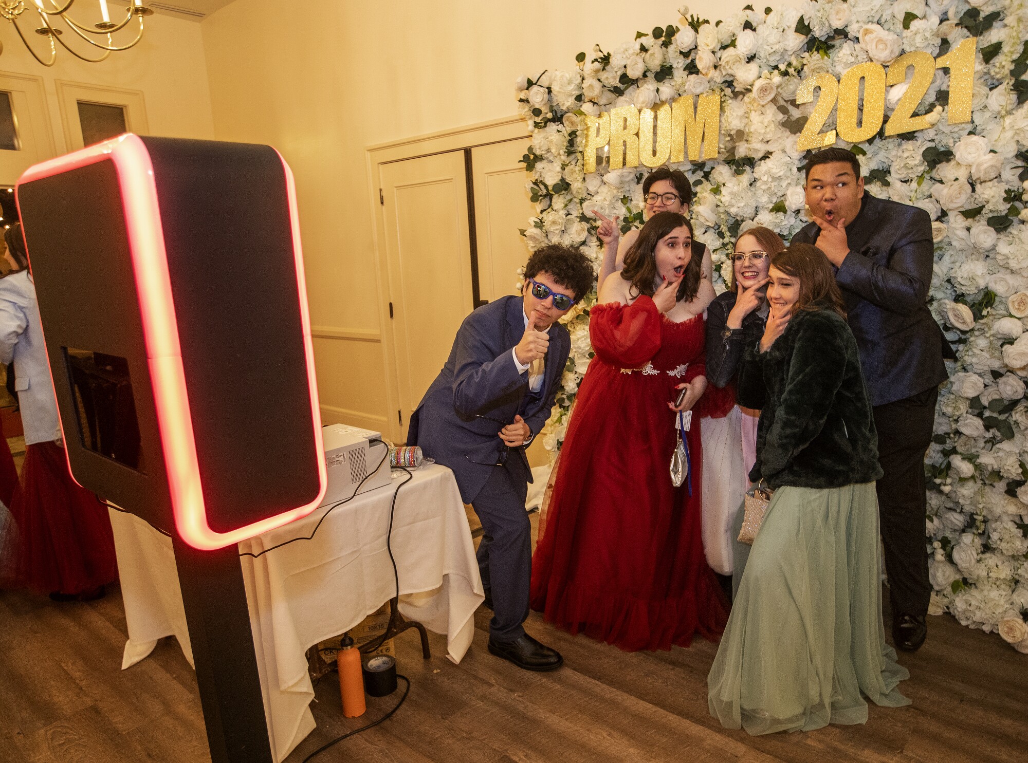 Teens stand in front of a flower backdrop that says "Prom 2021" and take a photo