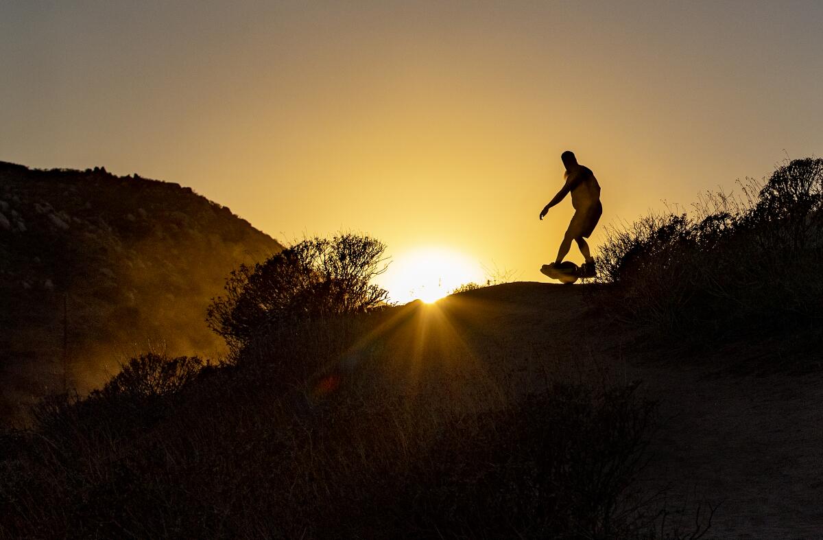 A man on an electric skateboard silhouetted by the sun behind a ridgetop