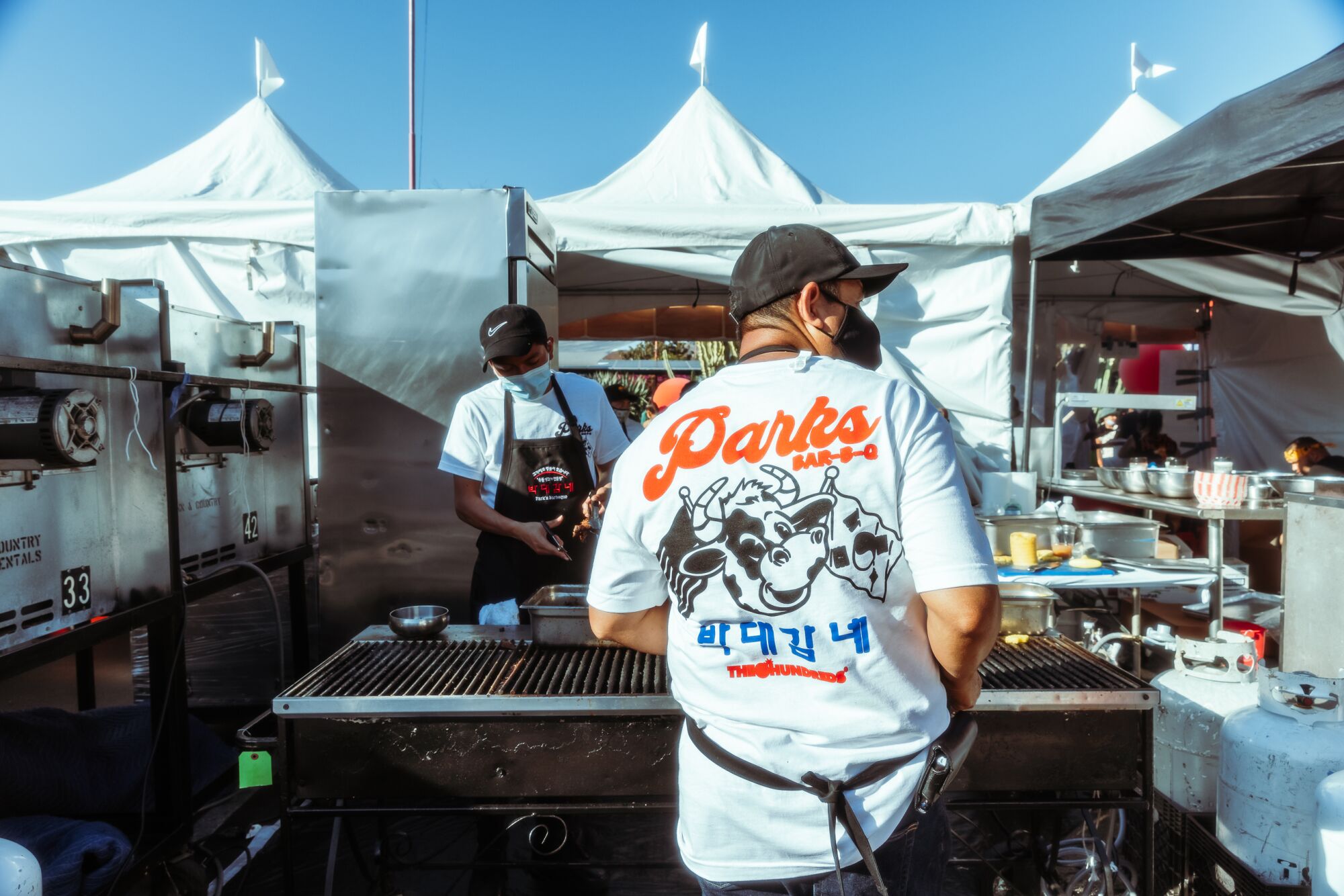 A man in a Park BBQ T-shirt stands on a grill.