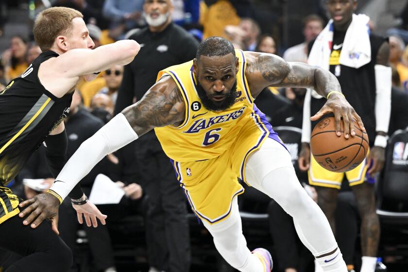 Lakers forward LeBron James leans down and dribbles around Warriors guard Donte DiVincenzo 