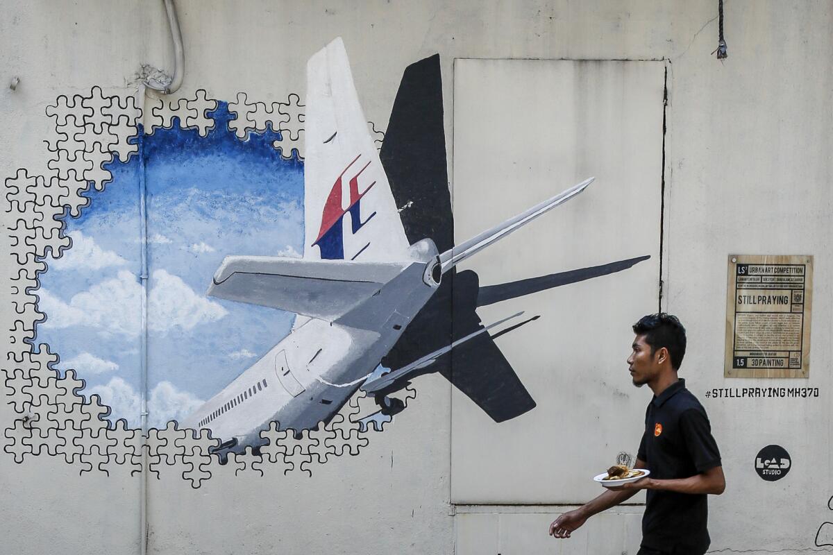 A waiter walks past a mural of flight MH370 in Shah Alam outside Kuala Lumpur, Malaysia. The Malaysian government said that two more pieces of debris, discovered in South Africa and Rodrigues Island off Mauritius, were "almost certainly" from Flight 370.